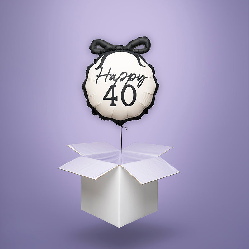 Czarno-biały balon foliowy w kształcie medalionu z kokardą i napisem „Happy 40”, wypełniony helem i wyskakujący z białego kartonu – stylowy prezent na 40. urodziny.