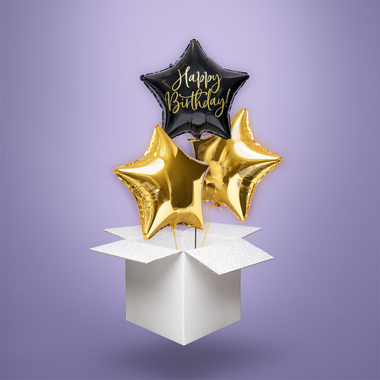 Czarny balon foliowy w kształcie gwiazdy z napisem „Happy Birthday” oraz dwie złote gwiazdy, wypełnione helem i wyskakujące z białego kartonu – stylowa niespodzianka urodzinowa.