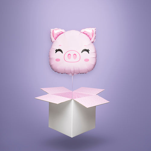 Balon foliowy w kształcie różowej świnki z uśmiechniętą buźką, unoszący się na wstążce nad otwartym białym kartonem, na fioletowym tle. Wysyłka Polska.