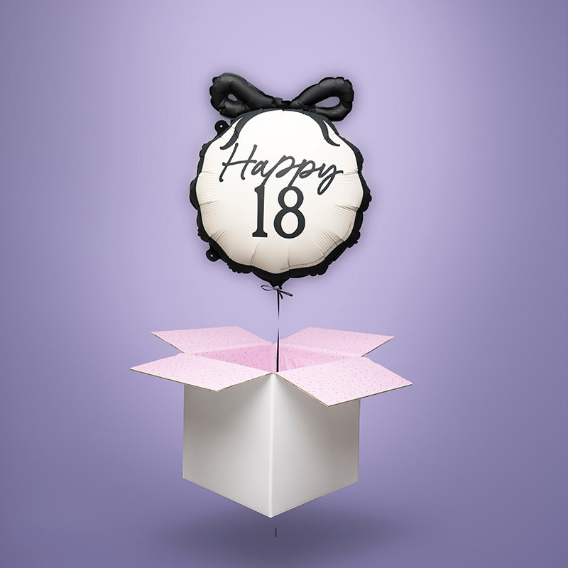 Balon z helem na 18. urodziny „Happy 18” unoszący się nad otwartym pudełkiem z różowym wnętrzem na fioletowym tle