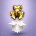 Trzy złote balony foliowe w kształcie serc, wypełnione helem i wyskakujące z białego kartonu – elegancka niespodzianka na Walentynki, rocznicę lub ślub.